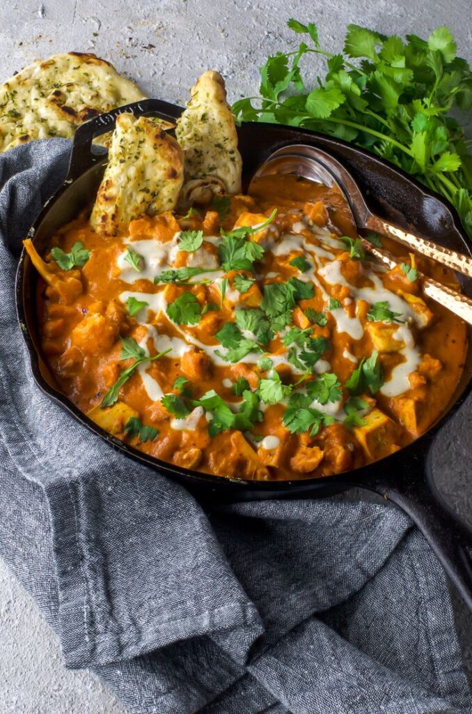 Creamy butter chicken in a skillet, garnished with cilantro, served with naan on the side.