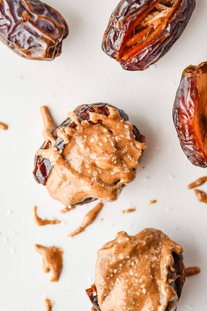 Dates topped with creamy almond butter and sea salt on a white background. Perfect healthy snack idea.
