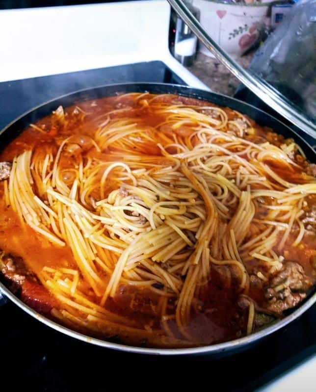 Pan of spaghetti cooking in rich tomato sauce on a stove.
