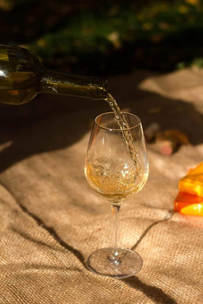 Pouring white wine into a glass on burlap surface in warm sunlight.