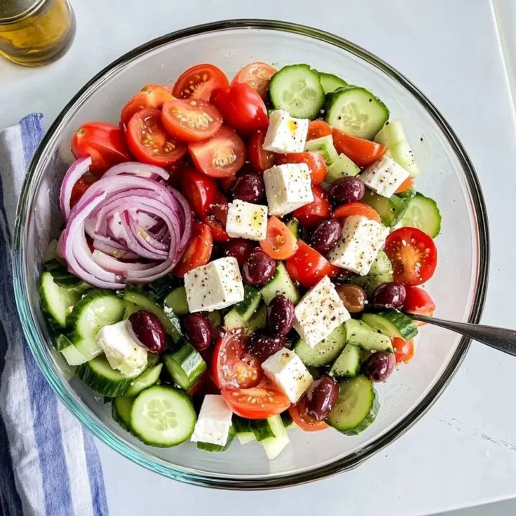 Colorful Greek salad with cherry tomatoes, cucumbers, red onions, feta, and olives in a glass bowl.