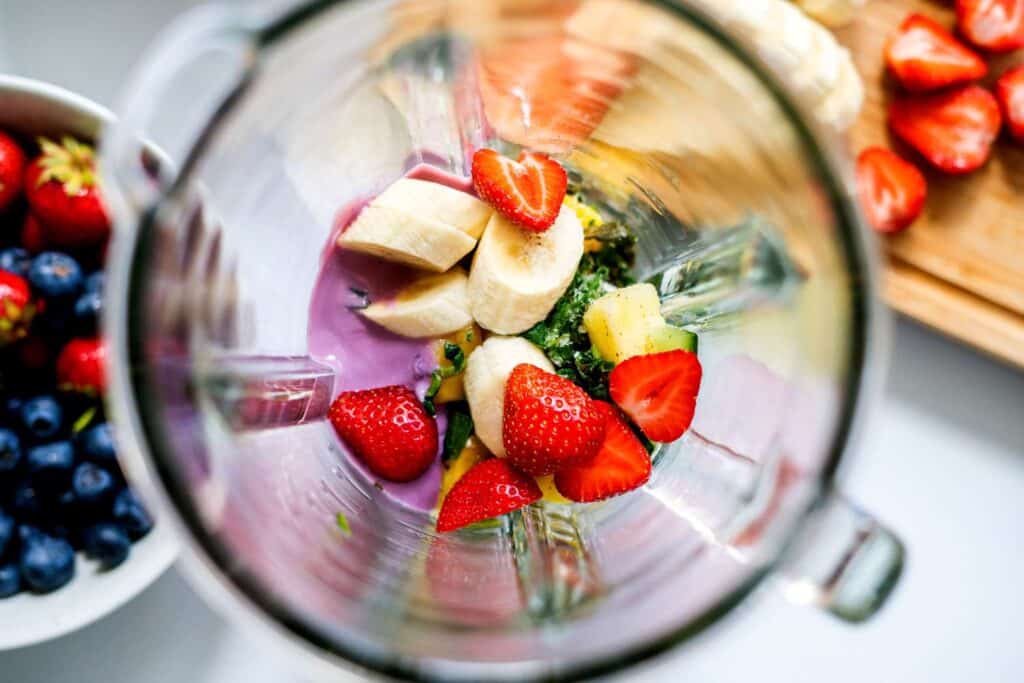 Blender with fresh strawberries, bananas, and blueberries, ready to make a colorful fruit smoothie.
