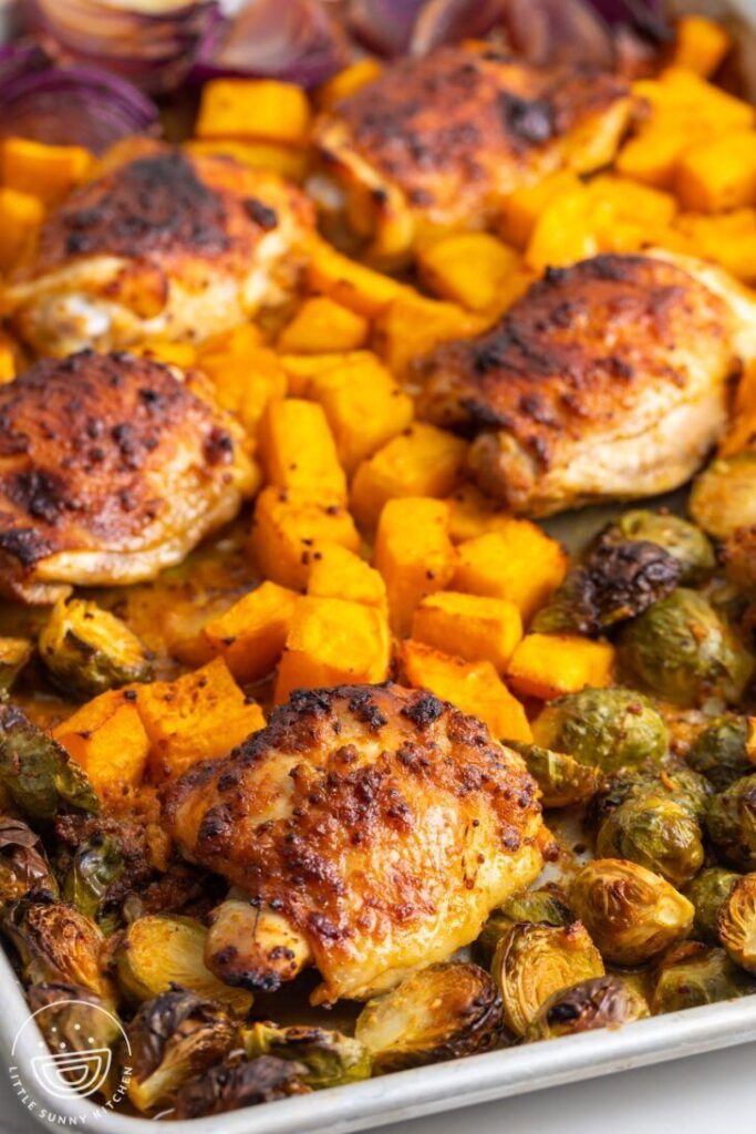 Roasted chicken thighs with butternut squash and Brussels sprouts on a baking sheet.