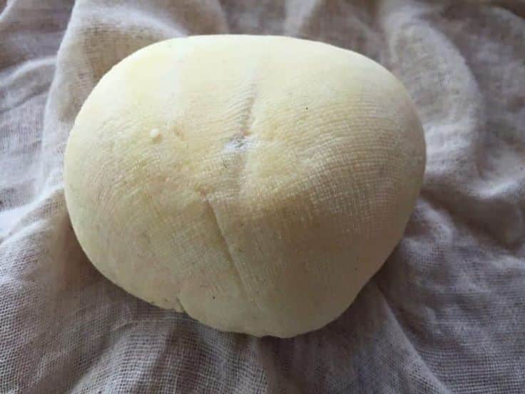 Round cheese wrapped in cloth on textured surface, showcasing homemade dairy craftsmanship.