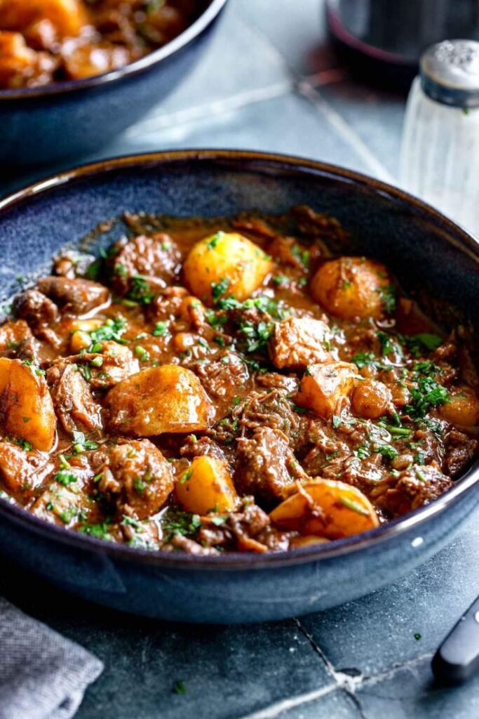 Hearty beef stew with potatoes, herbs, and rich sauce in a blue bowl. Perfect comfort food dish for cozy evenings.