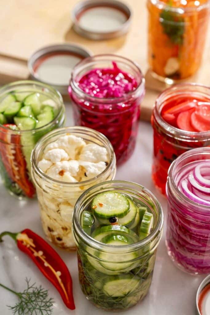 Jars of colorful pickled vegetables, including cucumbers, onions, and cauliflower, on a kitchen countertop.