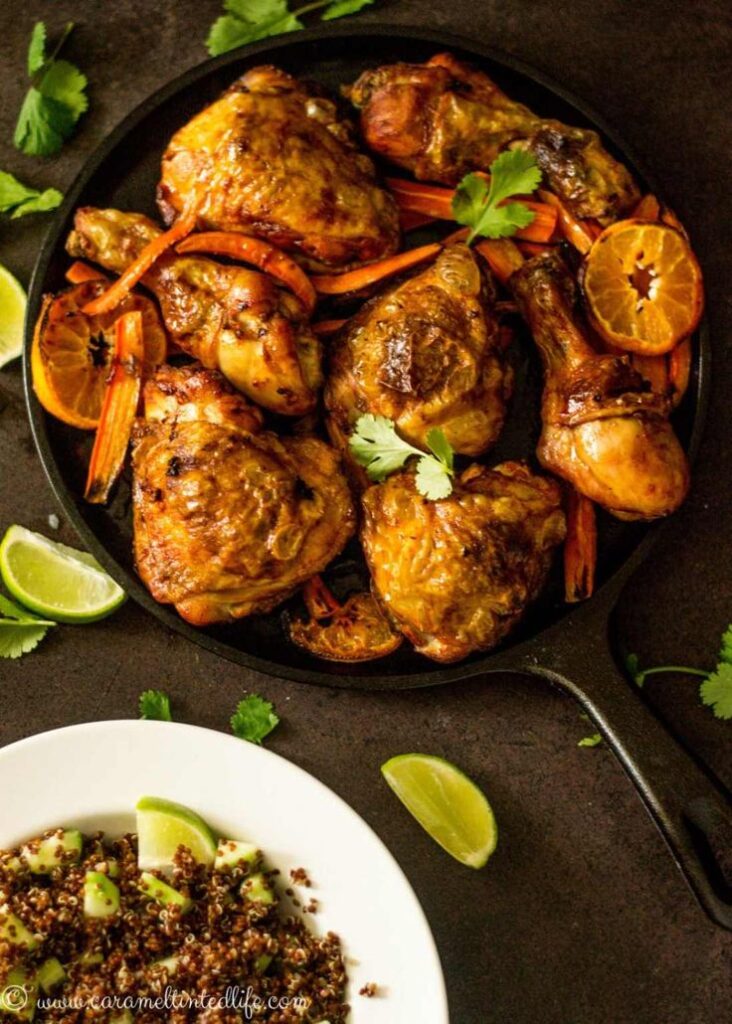 Roasted chicken and vegetables in a skillet with a side of quinoa and sliced lime.