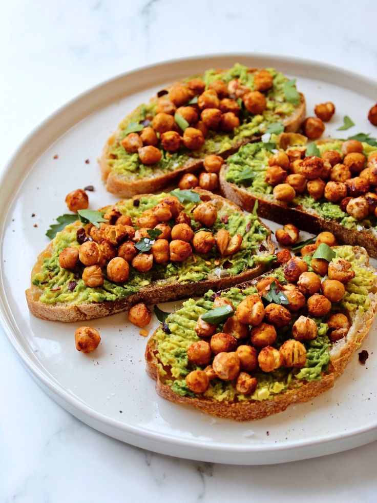 Avocado toast topped with crispy chickpeas and fresh herbs on a white plate. Perfect for a healthy breakfast or snack.