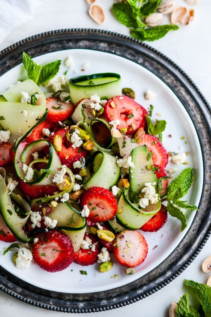 Fresh cucumber strawberry salad with feta, mint, and pistachios on a white plate.