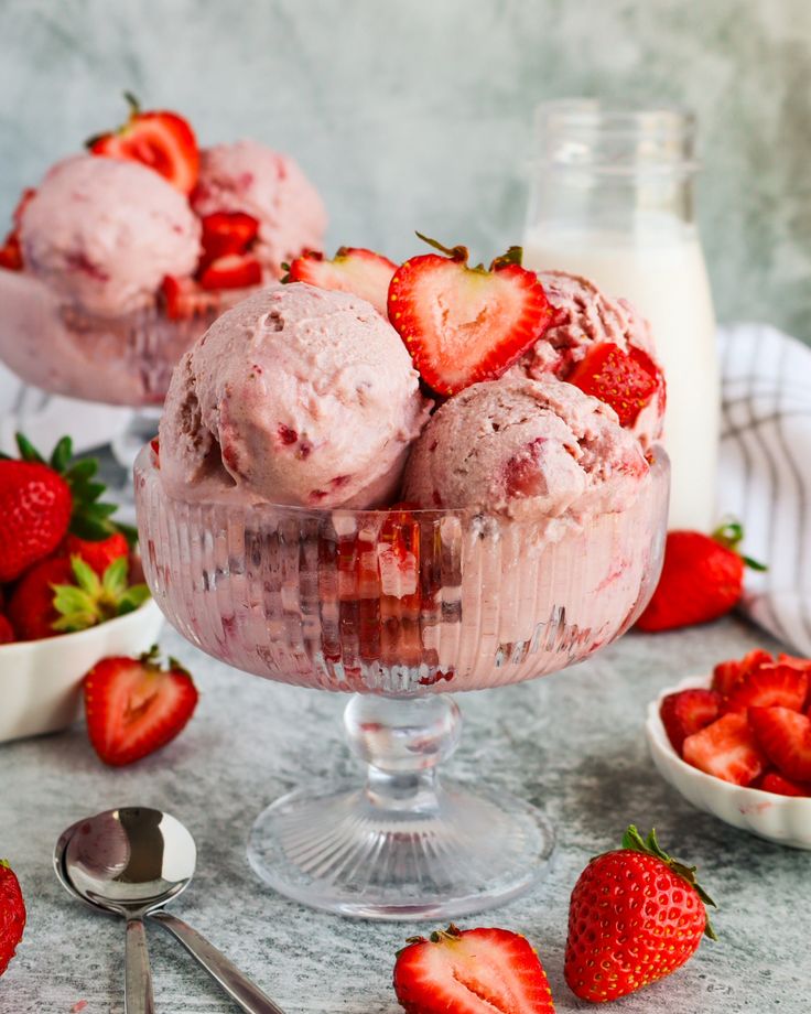 Strawberry ice cream scoops in a glass bowl with fresh strawberries, a summer dessert scene with milk in the background.