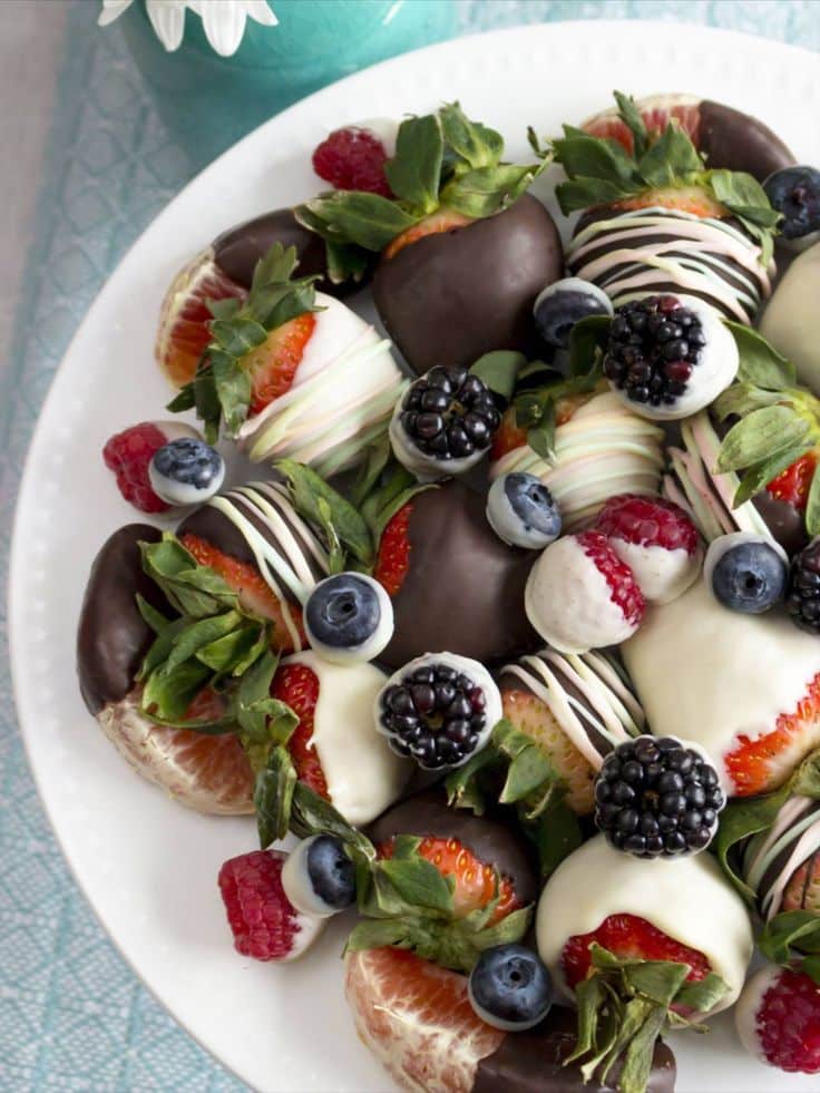 Plate of chocolate-covered strawberries with assorted berries and citrus slices. Delicious and colorful fruit dessert.