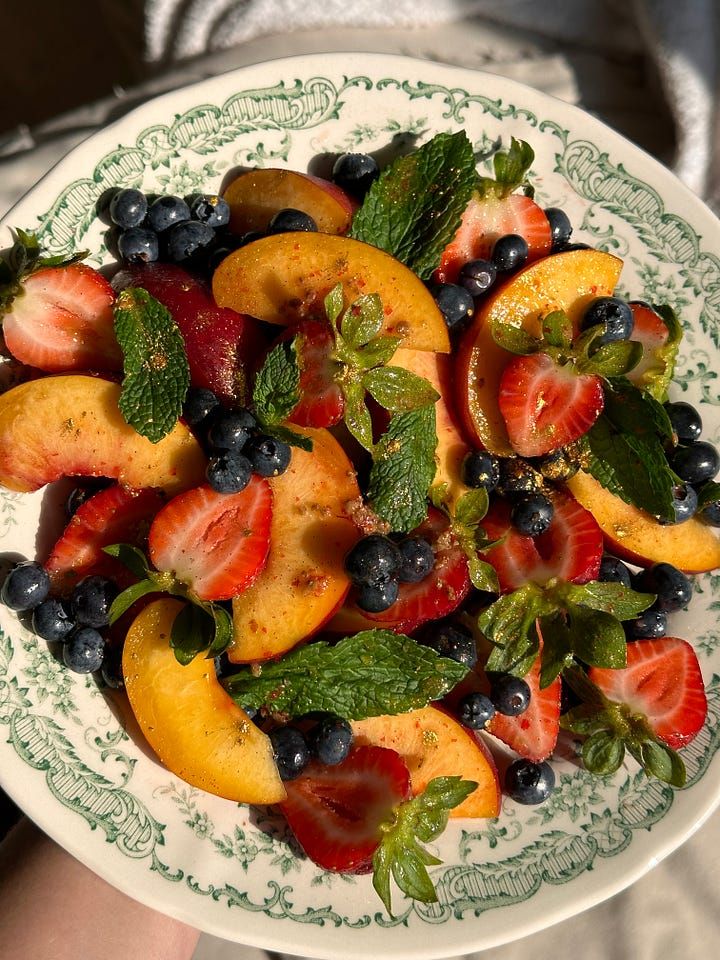 Fresh fruit salad with sliced peaches, strawberries, blueberries, and mint leaves on a decorative white plate.