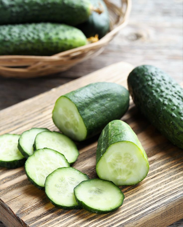 Fresh cucumbers sliced on a wooden board with whole cucumbers in a basket. Perfect for salads or snacks.