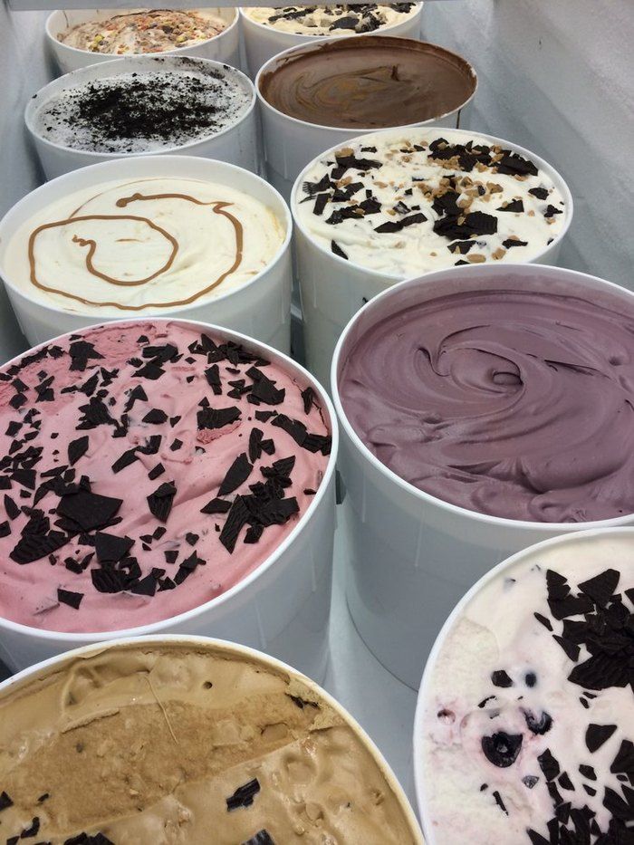 Assorted ice cream tubs with various flavors and toppings like chocolate chips, displayed in a white freezer.