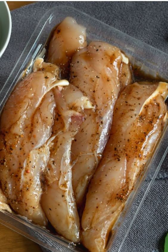 Marinated chicken breasts in a clear container, ready for cooking.