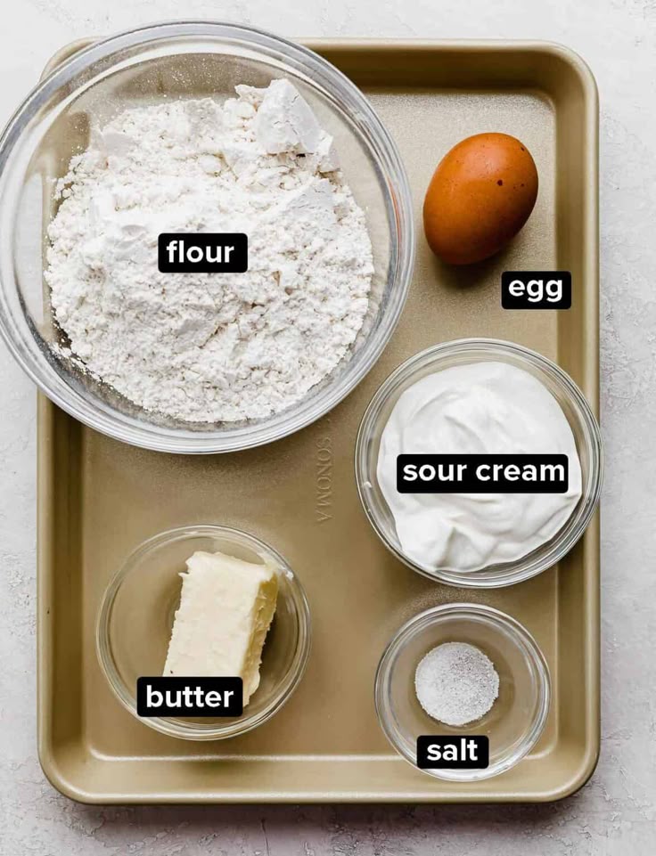 Baking ingredients on a tray: flour, egg, sour cream, butter, and salt. Perfect for pastry or cake preparation.