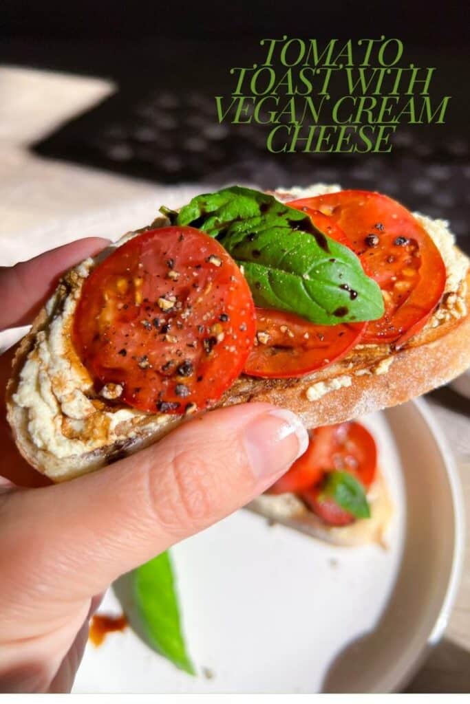 Tomato toast with vegan cream cheese, basil, and black pepper in hand. Fresh, healthy brunch snack.