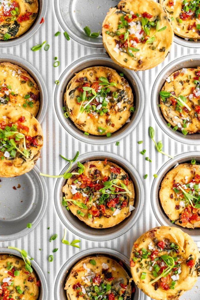 Freshly baked savory muffins with herbs and sun-dried tomatoes in a muffin pan, garnished with green onions.