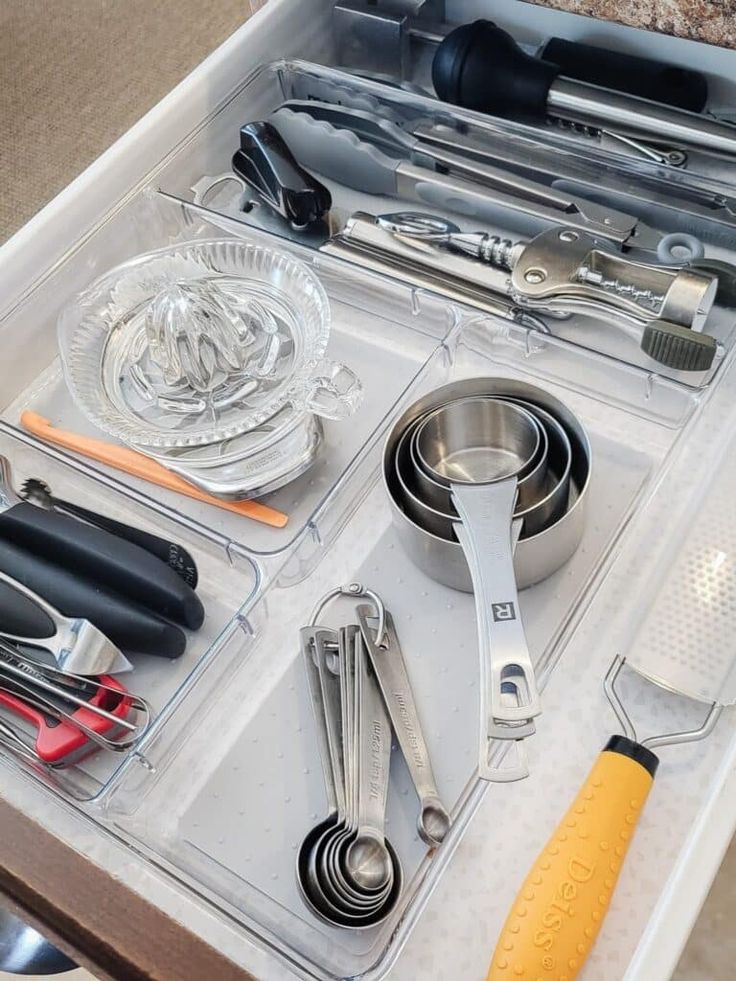 Open kitchen drawer with organized utensils: measuring cups, spoons, can opener, citrus juicer, and grater.