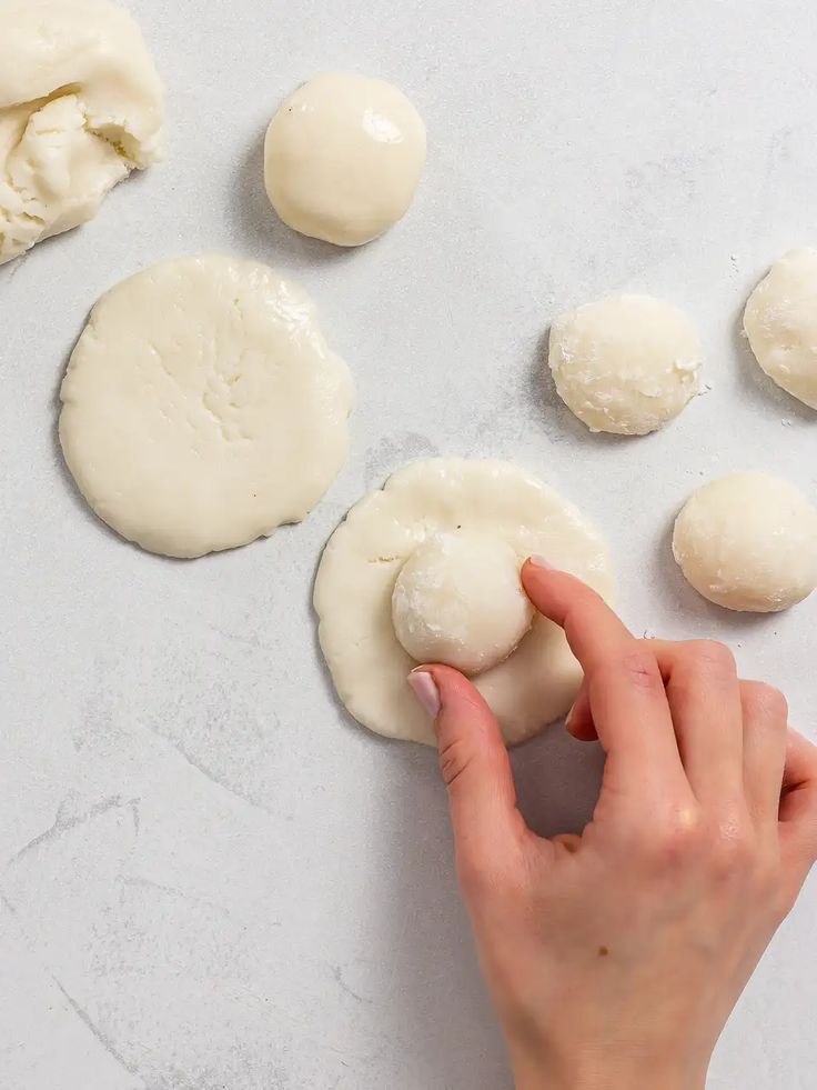 Hand shaping dough balls on a white surface for baking preparation.