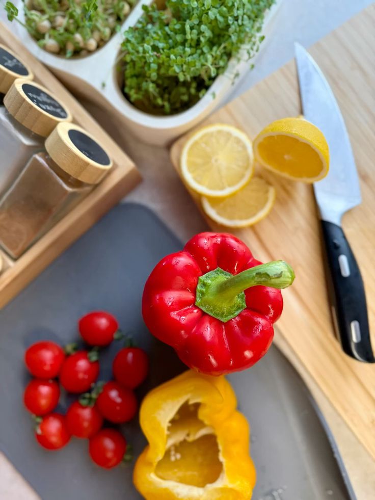 Fresh vegetables and herbs on cutting board with spices and knife. Red pepper, cherry tomatoes, and lemon slices.