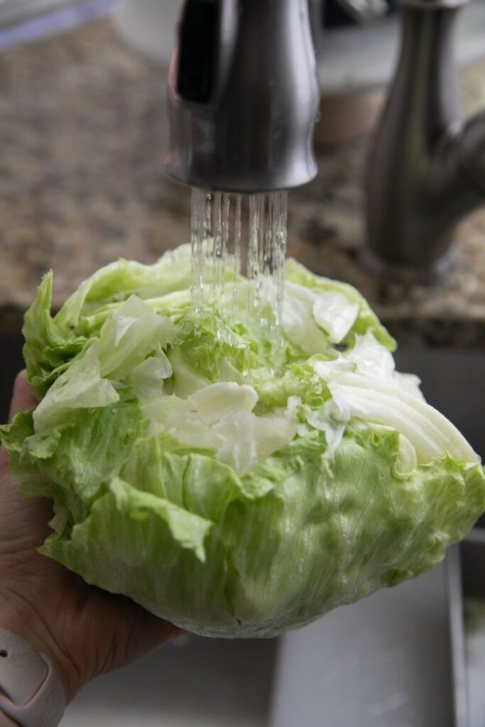Washing fresh iceberg lettuce under a kitchen faucet for a healthy meal preparation.