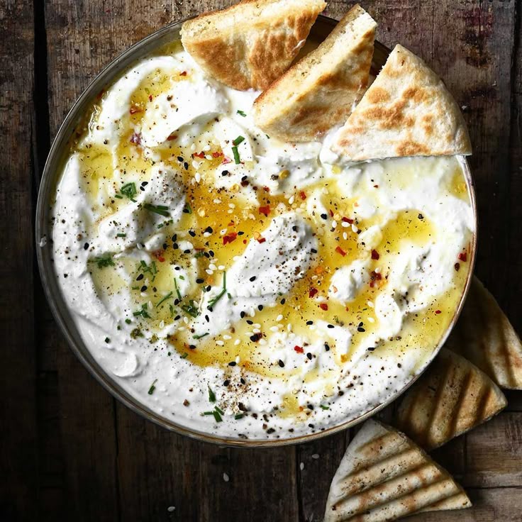 Creamy yogurt dip with herbs, olive oil, and spices, served with grilled pita wedges on a rustic wooden table.