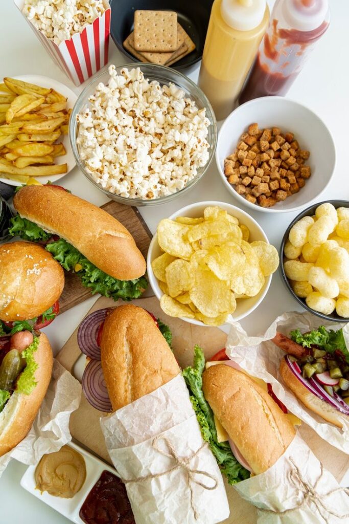 Assorted snacks including popcorn, fries, subs, chips, and sauces arranged on a table for a casual meal.