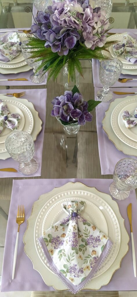 Elegant table setting with purple flowers, white plates, floral napkins, and crystal glasses for a special occasion.