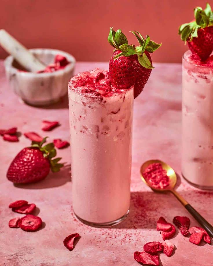 Icy strawberry milkshake with fresh berries and powder on a pink surface. Refreshing and delicious summer drink.