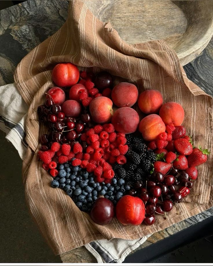 Assortment of fresh fruits including berries, peaches, and cherries on a rustic cloth, perfect for a vibrant display.