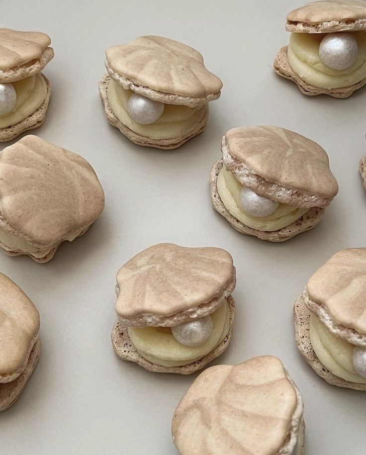 Shell-shaped macarons with creamy filling and pearl decor, arranged on a light surface. Perfect for elegant desserts.
