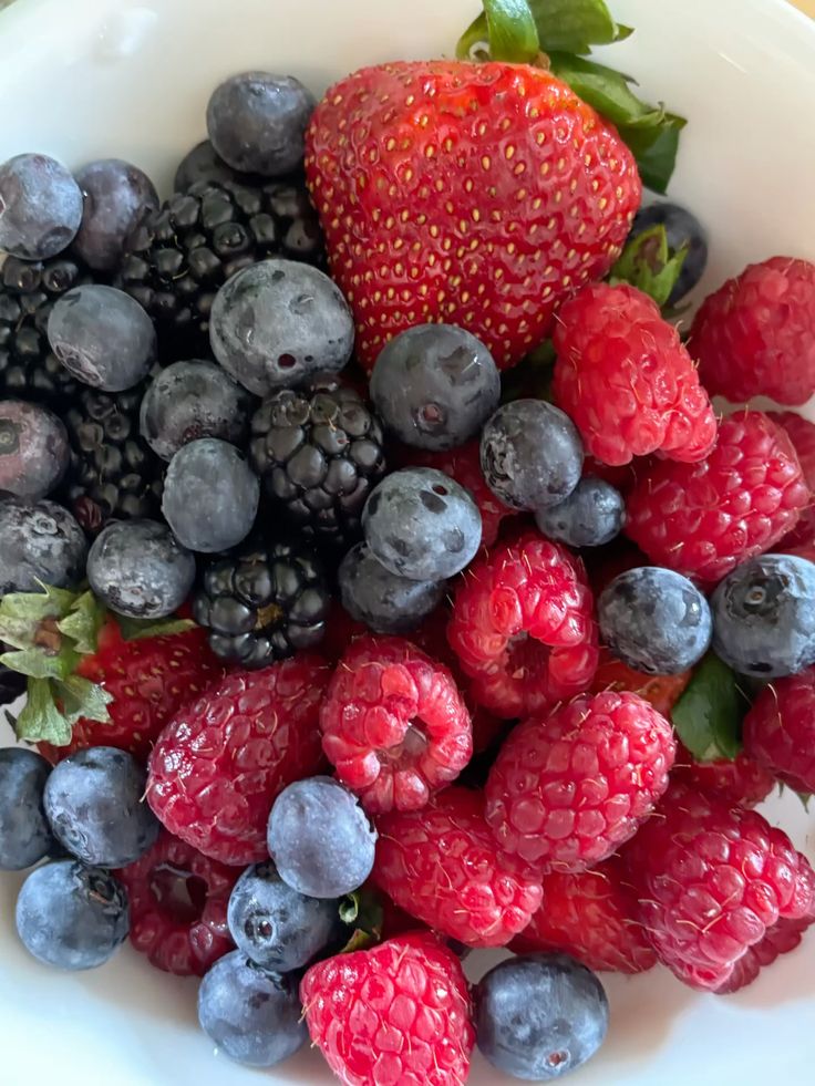 A colorful mix of fresh strawberries, blackberries, blueberries, and raspberries in a white bowl, perfect for a healthy snack.