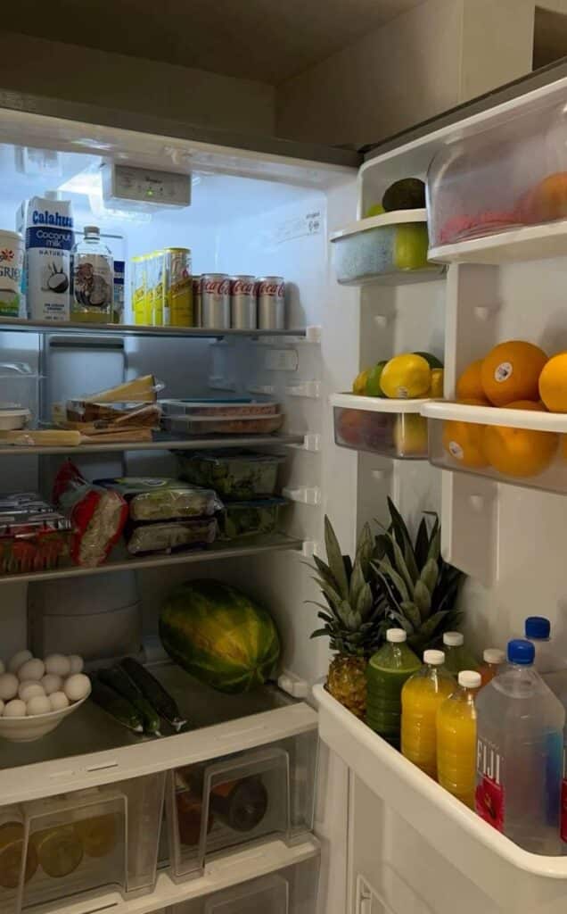Open fridge filled with beverages, fresh fruits, and groceries, showcasing a well-stocked kitchen.