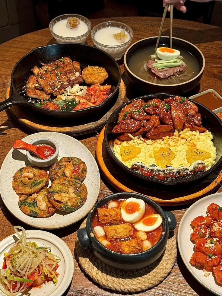 Assorted Korean dishes on a wooden table, featuring meats, soups, and banchan, creating a delicious dining experience.