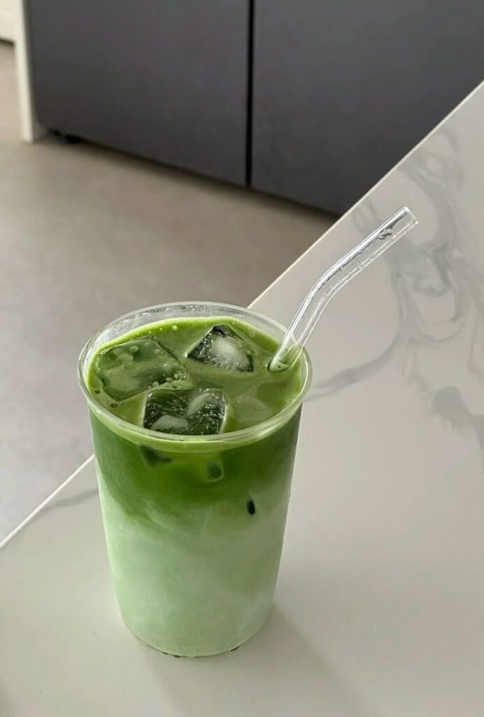 Iced matcha latte in a clear cup with a straw on a white table. Perfect refreshing green tea beverage.