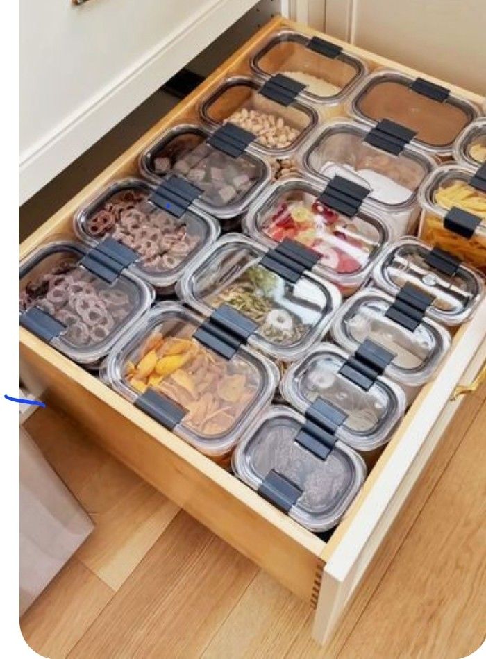 Organized kitchen drawer with transparent containers storing various snacks and dry ingredients neatly arranged.