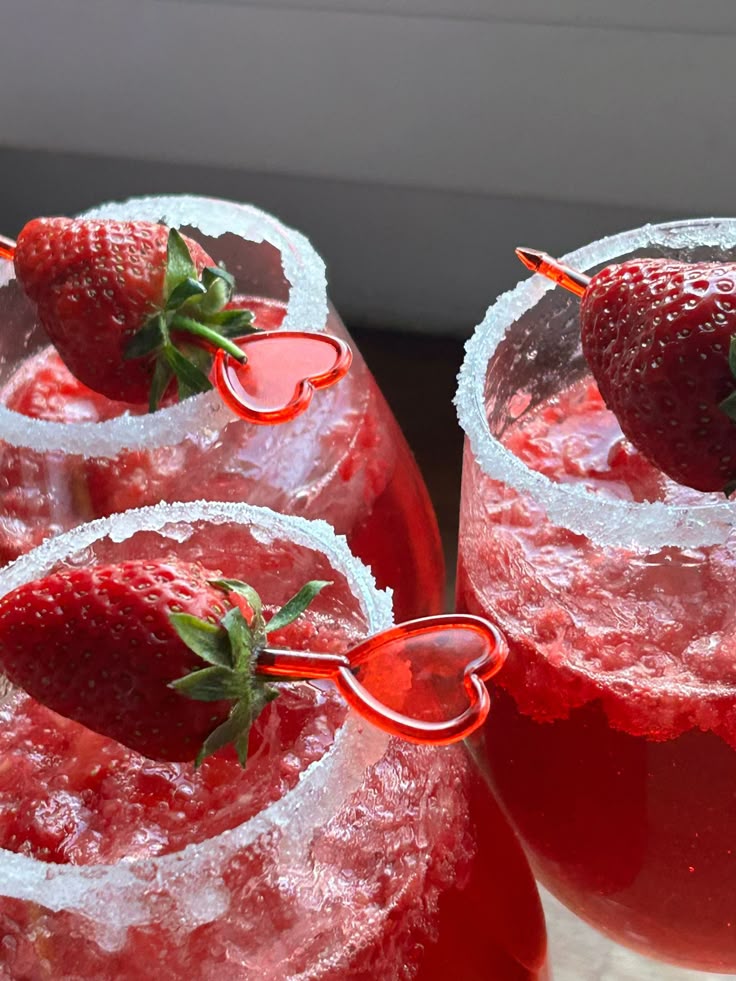 Red strawberry cocktails in sugar-rimmed glasses, garnished with fresh strawberries on heart-shaped skewers.