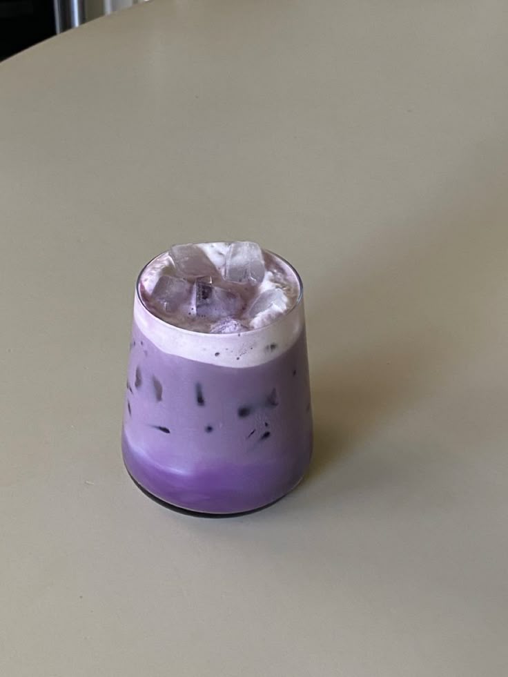 Iced purple yam latte with ice cubes in a glass on a light-colored table.