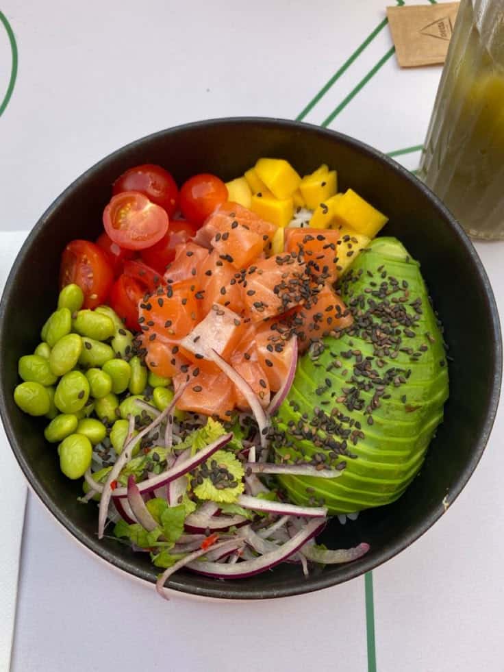 Colorful salmon poke bowl with avocado, edamame, cherry tomatoes, mango, red onion, and black sesame seeds.