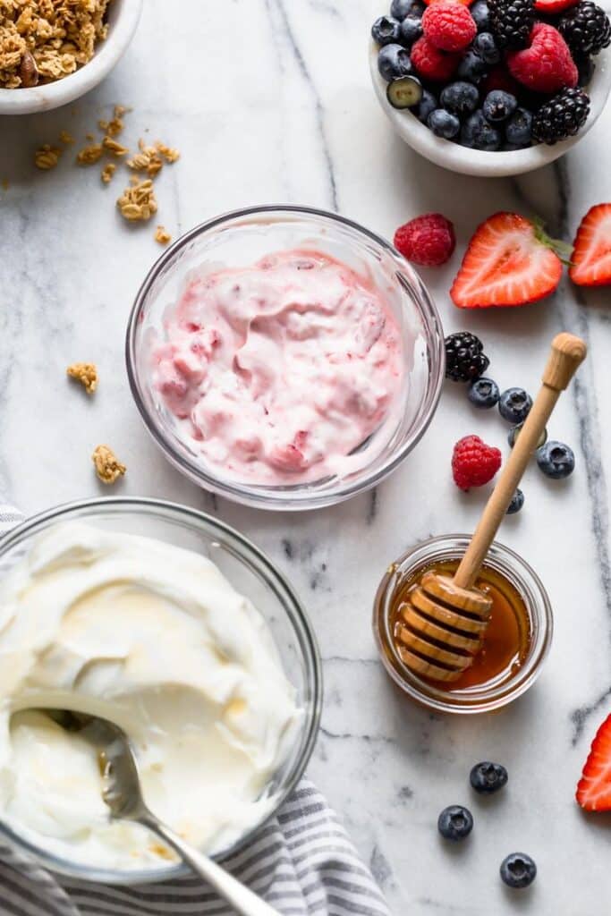 Bowl of yogurt with fresh berries, granola, and honey on a marble surface. Healthy breakfast ingredients.