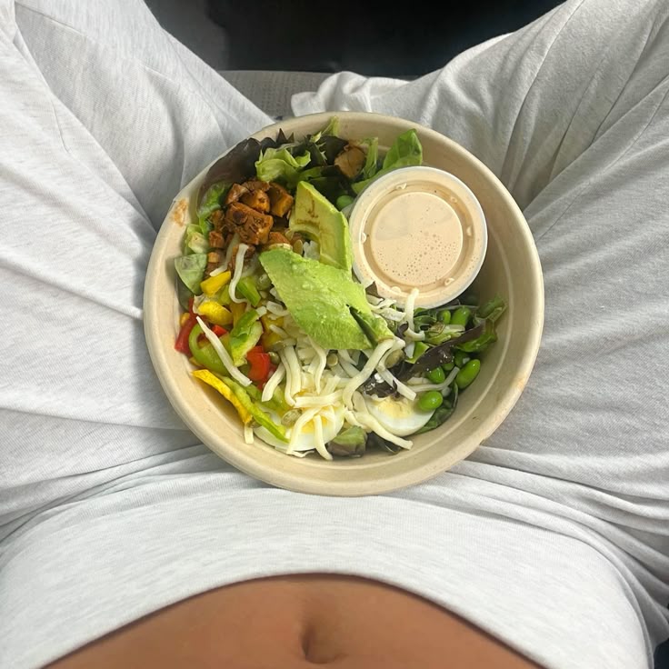 Healthy salad bowl on lap with avocado, edamame, cheese, and dressing, perfect for a nutritious meal on the go.
