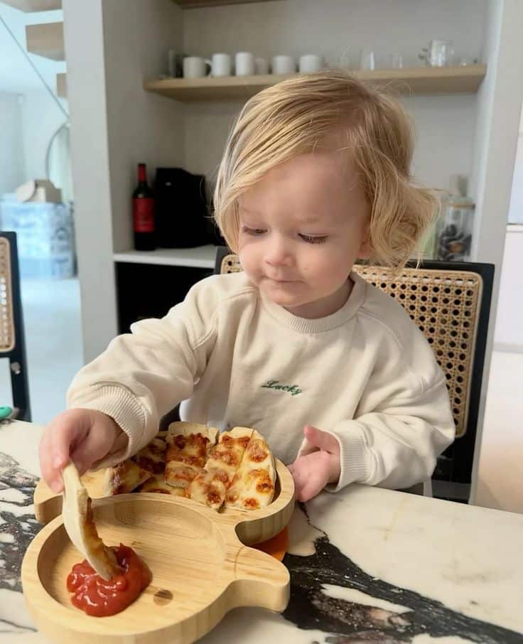 Toddler enjoying pizza slices and dipping sauce in a cozy kitchen setting.
