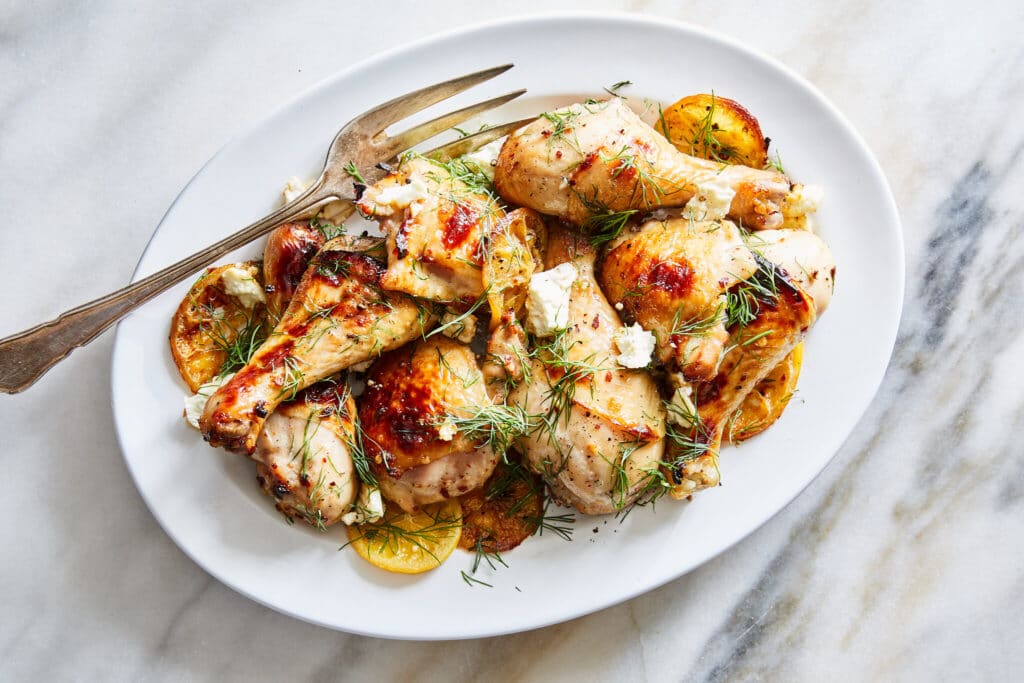 Grilled chicken drumsticks on a white plate garnished with fresh herbs and lemon slices.