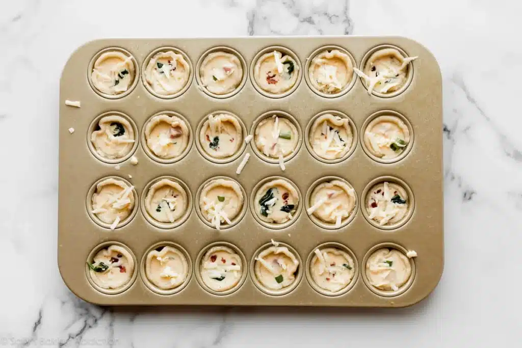 Mini quiche tray with cheese and herbs, ready to bake on a marble countertop. Ideal for brunch or parties.
