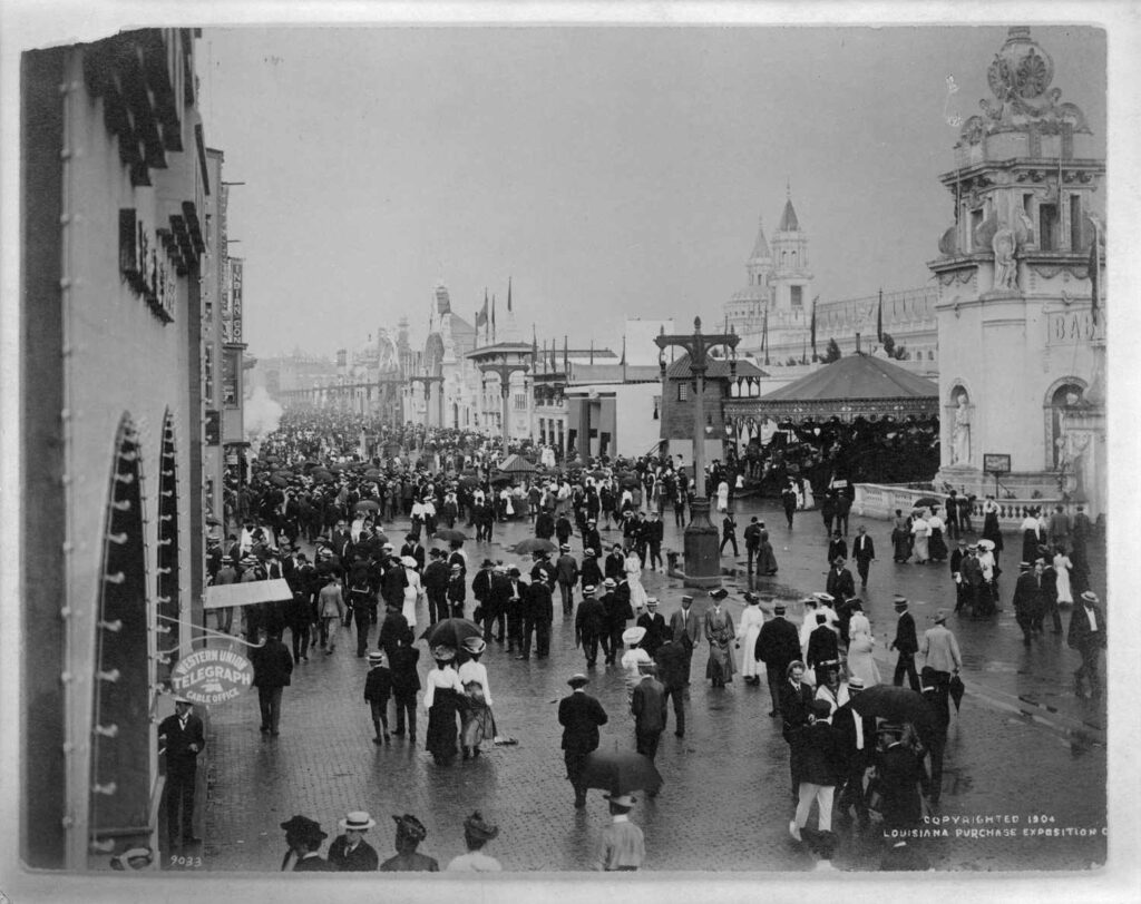 Crowd at the 1904 Louisiana Purchase Exposition in St. Louis, with historic architecture and bustling street scene.