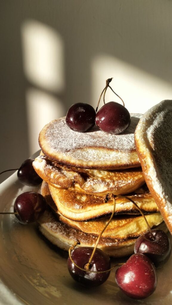 Fluffy pancakes stacked with cherries and powdered sugar in warm sunlight. Perfect breakfast treat.