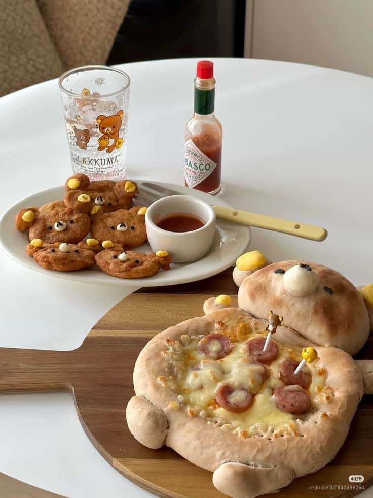 Bear-shaped pizza and cookies on a table with spicy sauce and a themed glass. Cute and fun food presentation.