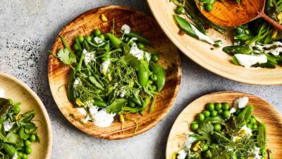 Fresh green salad with peas, herbs, and cream dressing on wooden plates, vibrant and healthy meal idea.