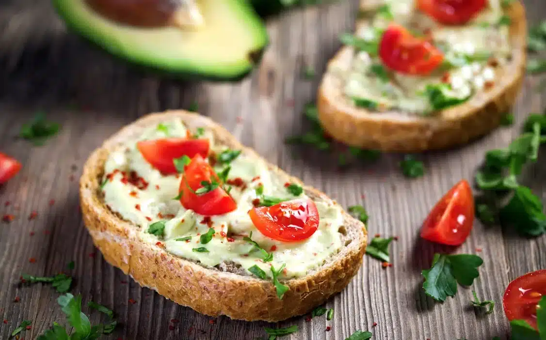 Avocado toast with cherry tomatoes and herbs on rustic bread, garnished with spices, on a wooden table.